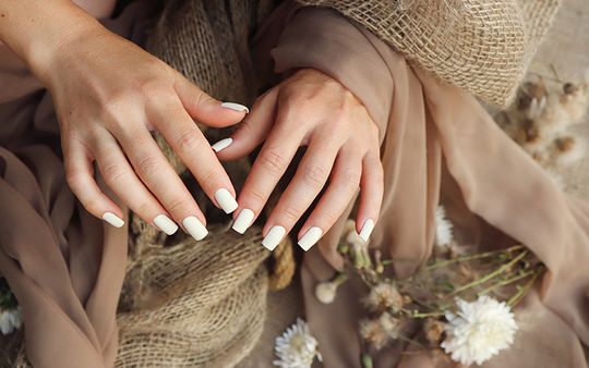 Lange weiße Fingernägel mit braunem Schal und Blumen